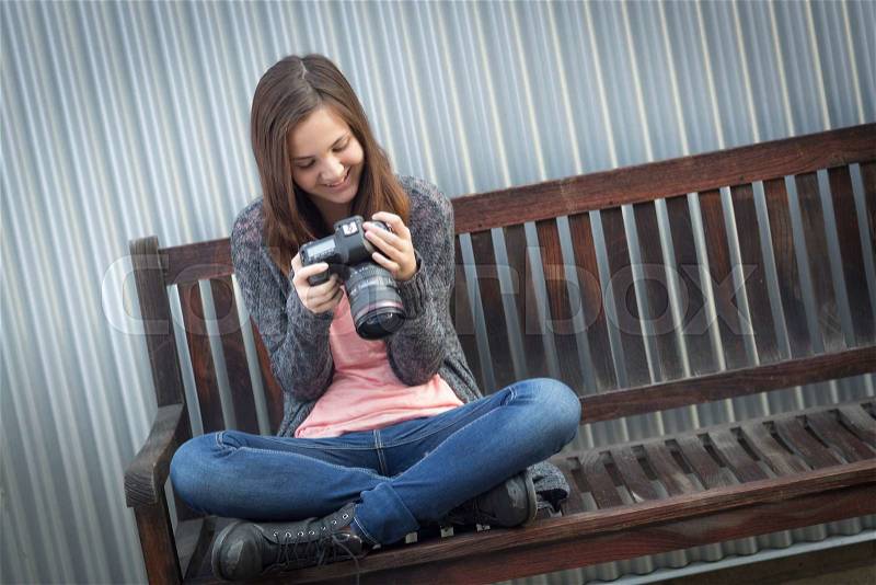 Young Girl Photographer Sitting on Bench Looking at Back of Camera, stock photo