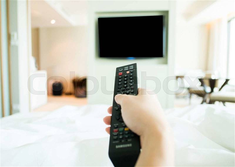 Hand using tv remote control in bed, stock photo