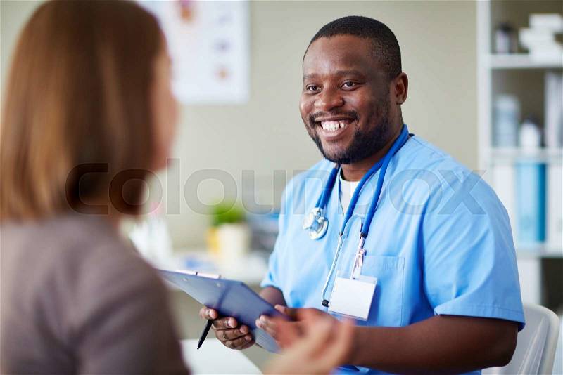 Smiling African doctor working with patient in his office, stock photo