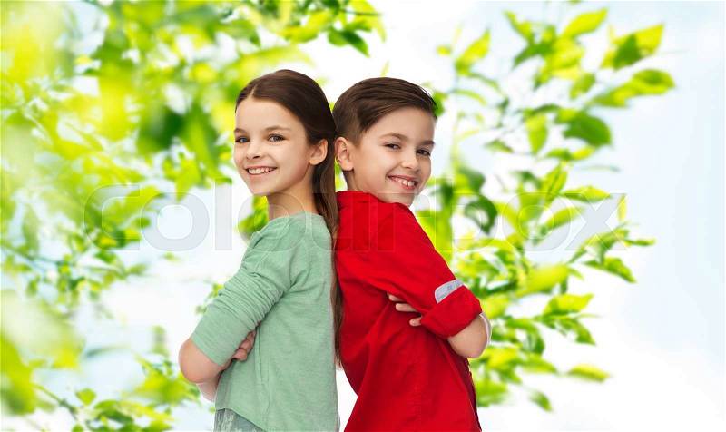 Childhood, summer, and people concept - happy smiling boy and girl standing back to back over green natural background, stock photo