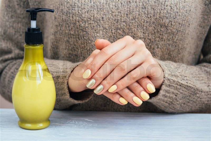 Woman in a brown sweater showing hands with yellow manicure, close-up, stock photo