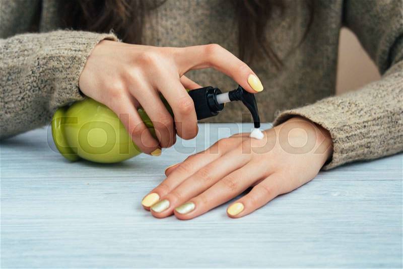 Girl in brown sweater with yellow manicure applying hand cream, close-up, stock photo