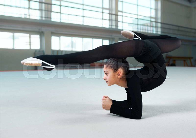 Side view of little girl practicing gymnastic in gym-hall, stock photo