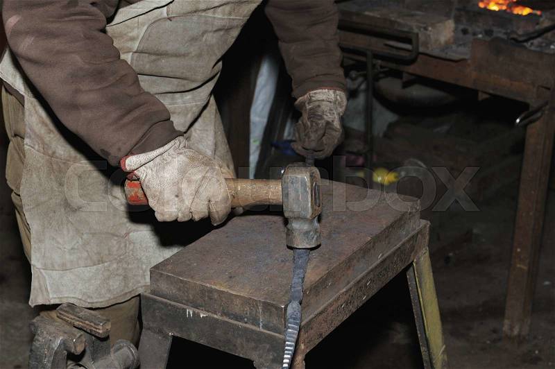 Blacksmith working metal with hammer on the anvil in the forge, stock photo