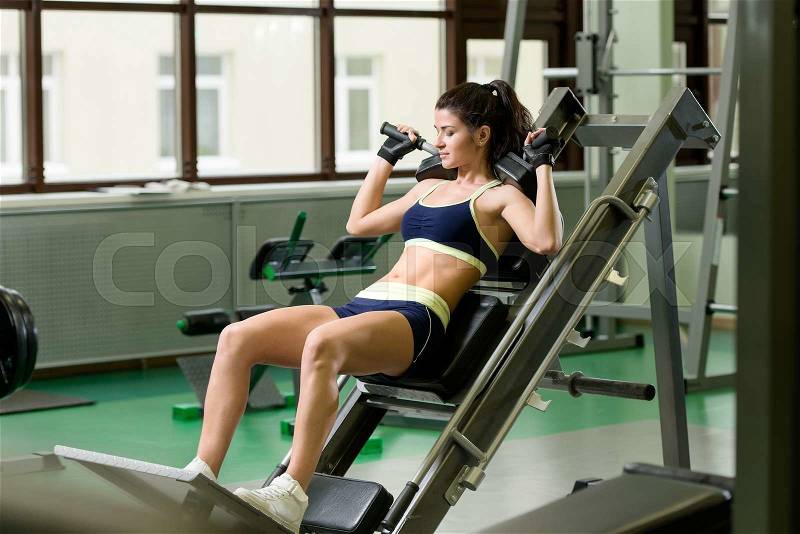 Young pretty woman pumping up muscles with training apparatus in fitness club, stock photo