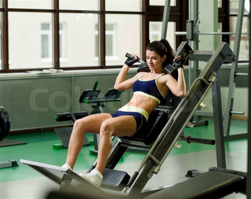 Young pretty woman pumping up muscles with training apparatus in fitness club, stock photo