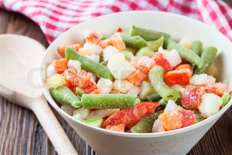 A mixture of assorted frozen vegetables in a bowl on brown wooden table, stock photo