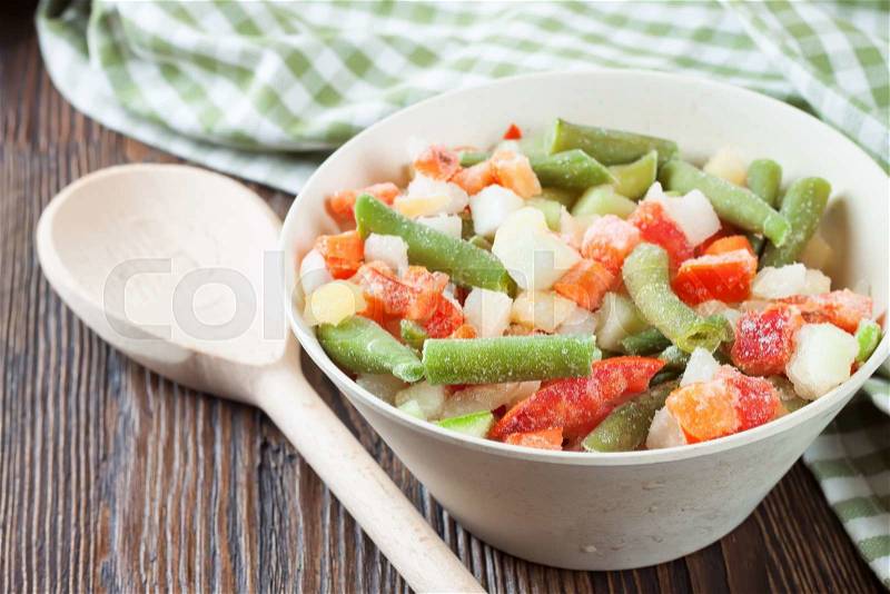 A mixture of assorted frozen vegetables in a bowl on brown wooden table, stock photo