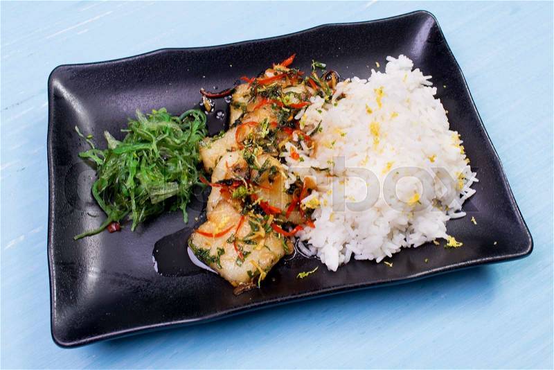 Rice, fried vegetables and fish. The finished dish on a wooden table, stock photo