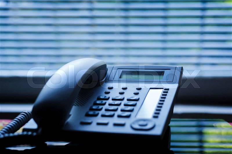 Executive VoIP desk phone with traditional corded headset and the business office window blinds in the background. Shallow depth of field - focus on the center of the phone, stock photo