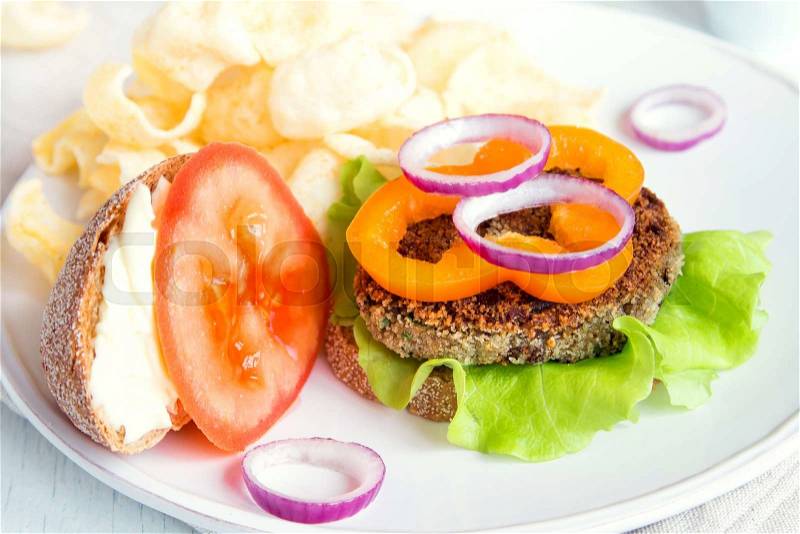 Vegetarian lentil burger with vegetables and chips on white plate, stock photo
