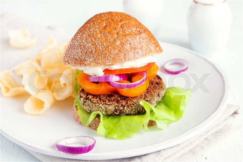 Vegetarian lentil burger with vegetables and chips on white plate, stock photo
