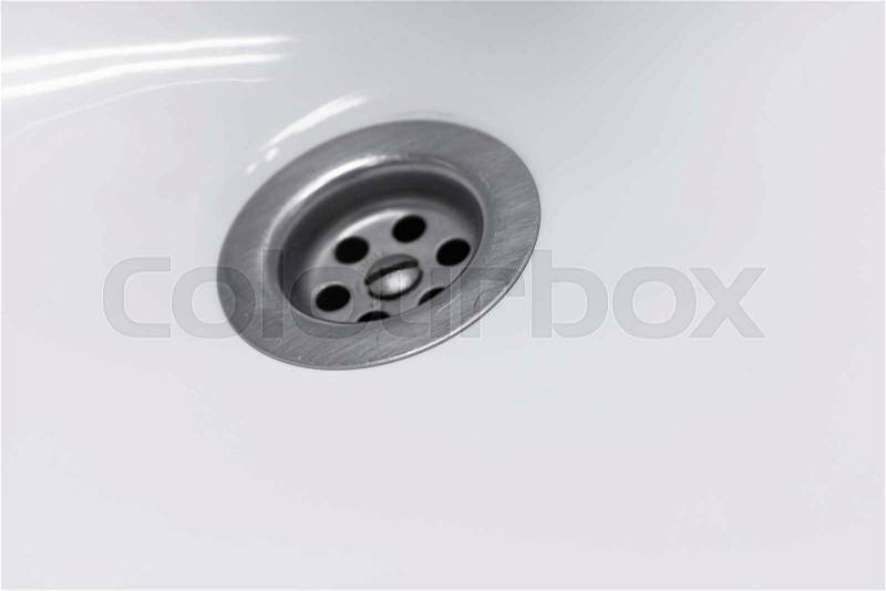 Standard round drain hole in white domestic sink, macro photo with selective focus, stock photo