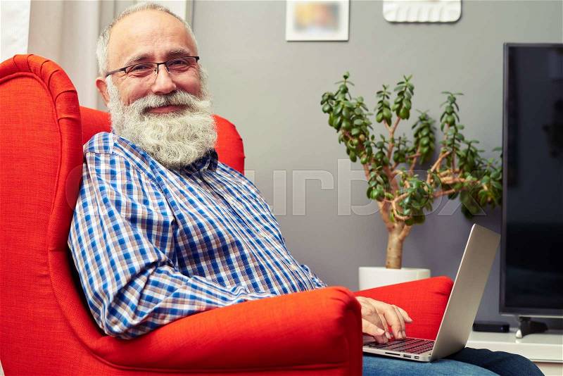 Smiley senior man working with laptop and looking at camera, stock photo