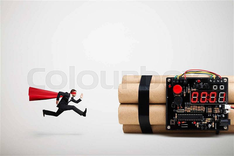 Superman in red cloak and mask ready to defusing big bomb with timer over light grey background, stock photo