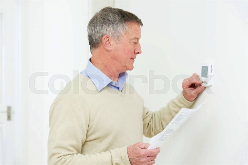 Worried Senior Man With Bill Turning Down Heating Thermostat, stock photo