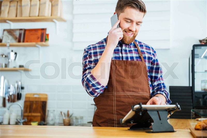 Barista taking order on cellphone and using tablet in cafeteria, stock photo