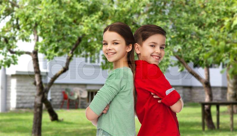 Childhood, fashion and people concept - happy smiling boy and girl standing back to back over private house backyard background, stock photo