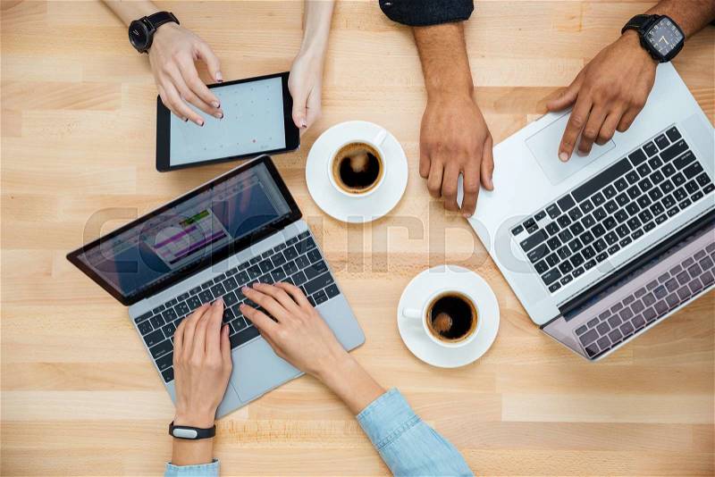 Top view of multiethnic group of young people using laptops and tablet and drinking coffee, stock photo