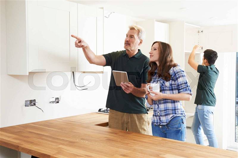 Woman With Carpenter Looking At Plans For Kitchen On Digital Tablet, stock photo