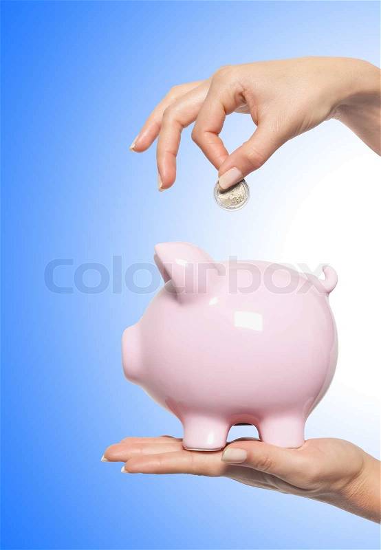 Hand putting money into the piggy bank over blue, stock photo