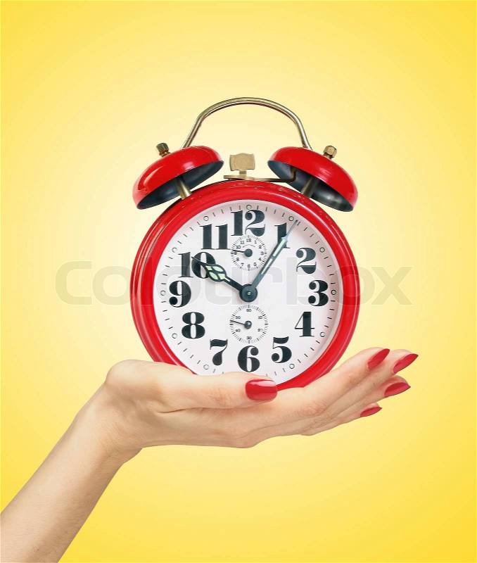 Red alarm clock in woman hand over yellow background, stock photo