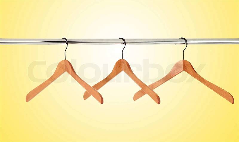 Wooden coat hangers on a clothes rail isolated on yellow background, stock photo