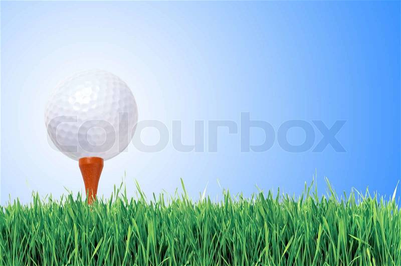 Golf ball with tee in the grass over blue sky, stock photo