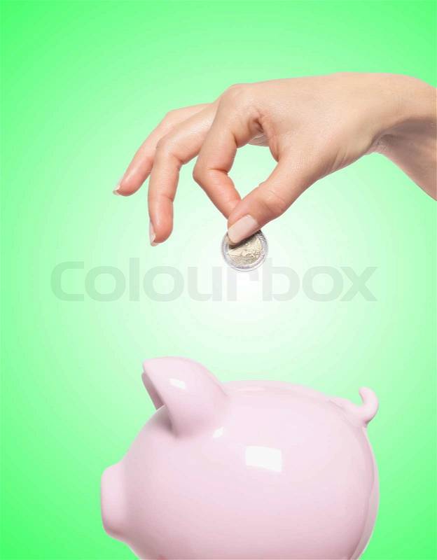 Hand putting money into the piggy bank over green background, stock photo