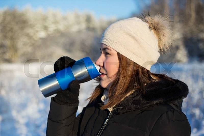 Frost concept - young beautiful woman with thermal mug in winter forest, stock photo