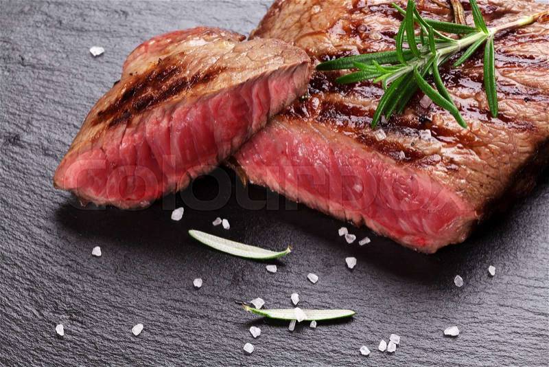 Grilled beef steak with rosemary, salt and pepper on black stone plate, stock photo