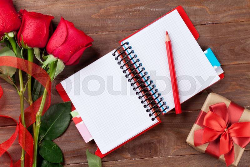 Valentines day roses, gift box and notepad over wooden background. Top view with copy space, stock photo