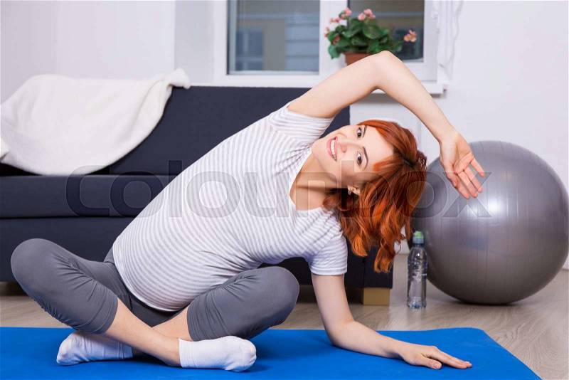 Young pregnant woman doing stretching exercises at home, stock photo