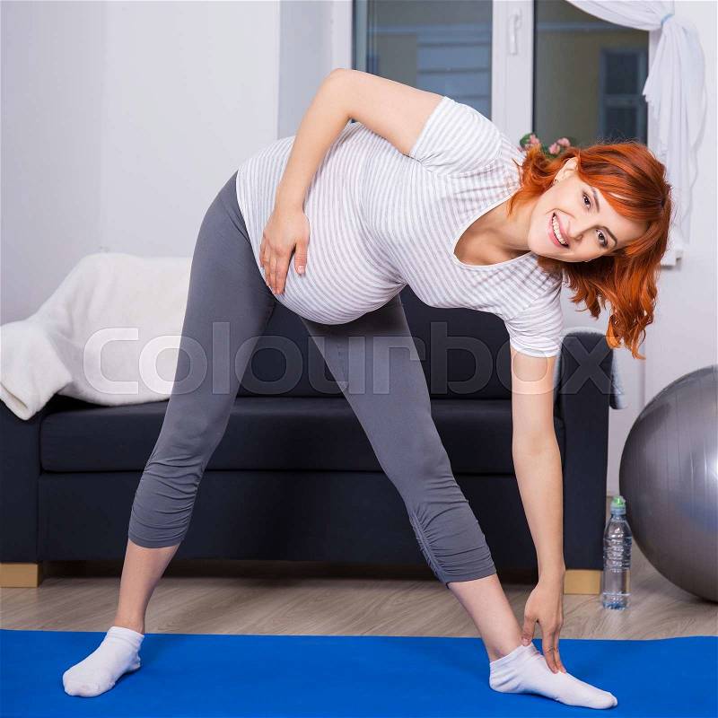 Sport and pregnancy concept - pregnant woman doing stretching exercises in living room at home, stock photo