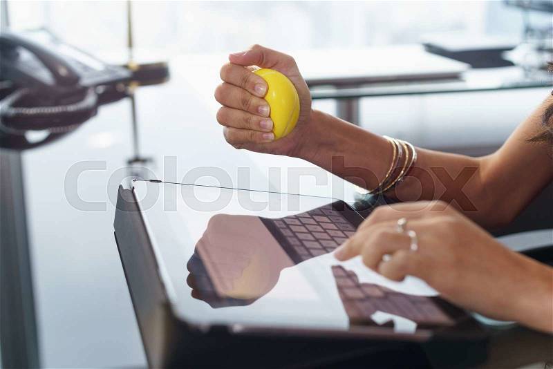 Office worker typing email on tablet computer. The woman feels stressed and nervous, holds an antistress yellow ball in her hand, stock photo