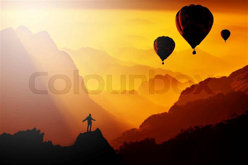 Silhouetted of man standing on mountain with hot-air balloons flying over the mountain when sunset or sunrise. Success concept, stock photo