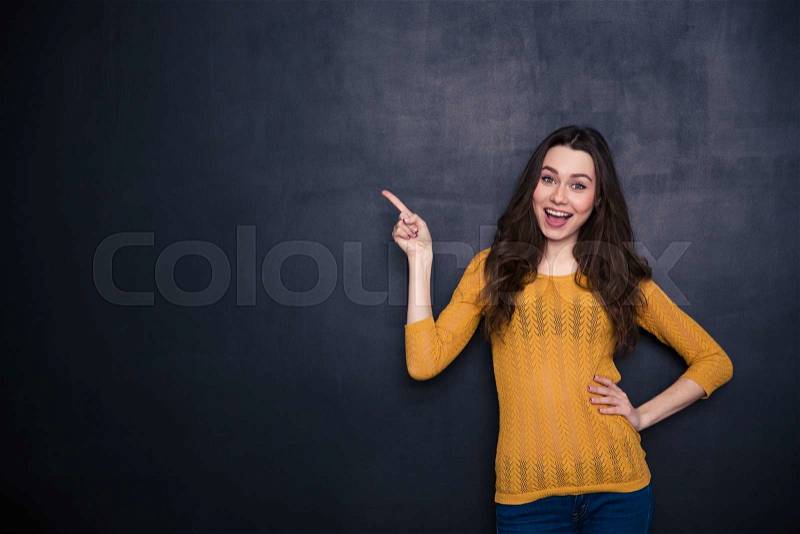 Cheerful casual woman pointing away over black background, stock photo