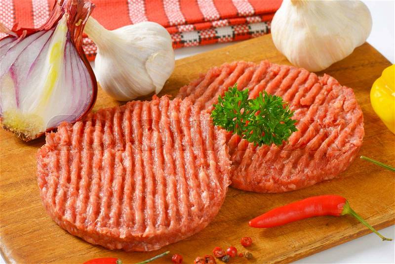 Raw hamburger patties and vegetables on cutting board, stock photo
