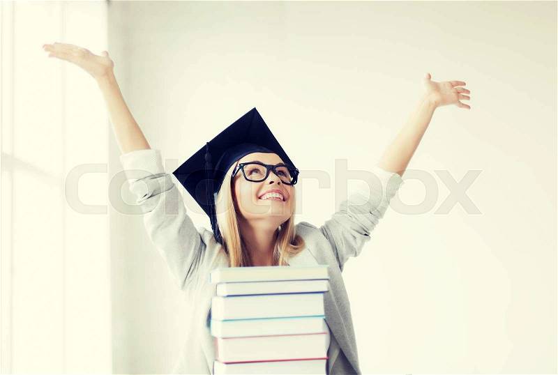 Happy student in graduation cap with stack of books, stock photo