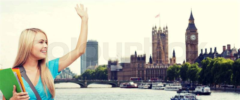 Education, school, study abroad, gesture and people concept - smiling student with folders waving hand over london city and thames river background, stock photo