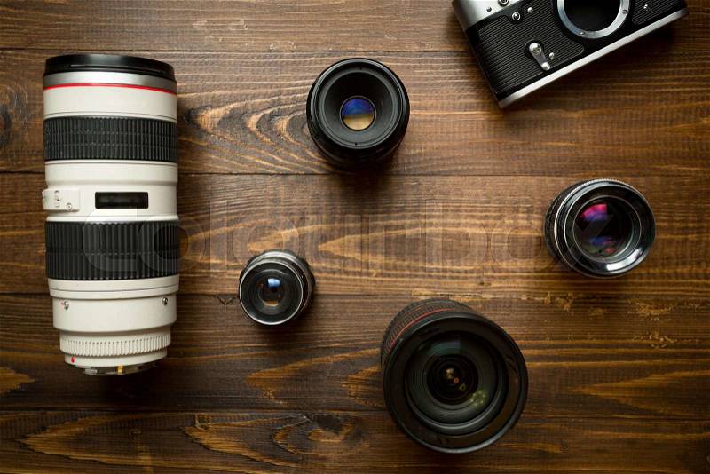 Vintage film camera and different lenses lying on wooden background, stock photo