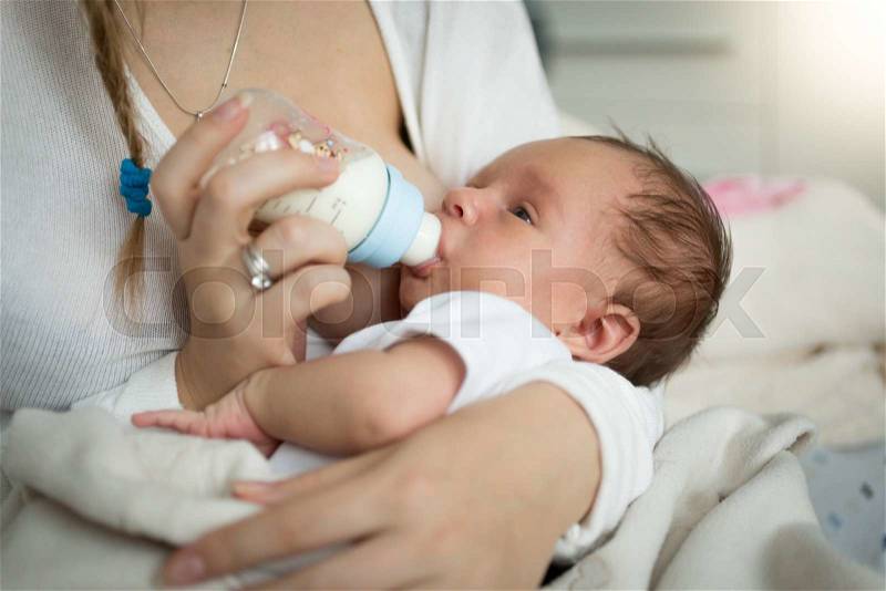 Closeup portrait of mother feeding newborn baby from bottle, stock photo