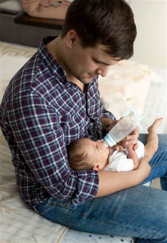 Toned portrait of young father feeding newborn son with milk, stock photo