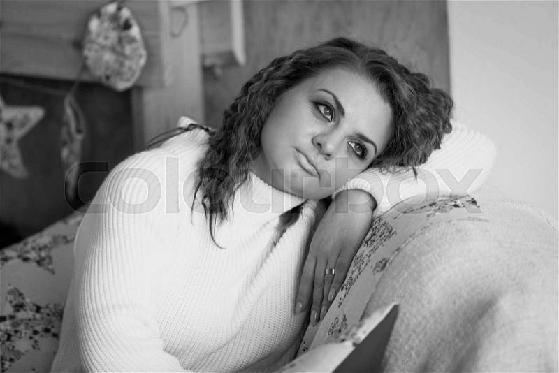 Black and white closeup portrait of cute woman in sweater sitting on sofa, stock photo