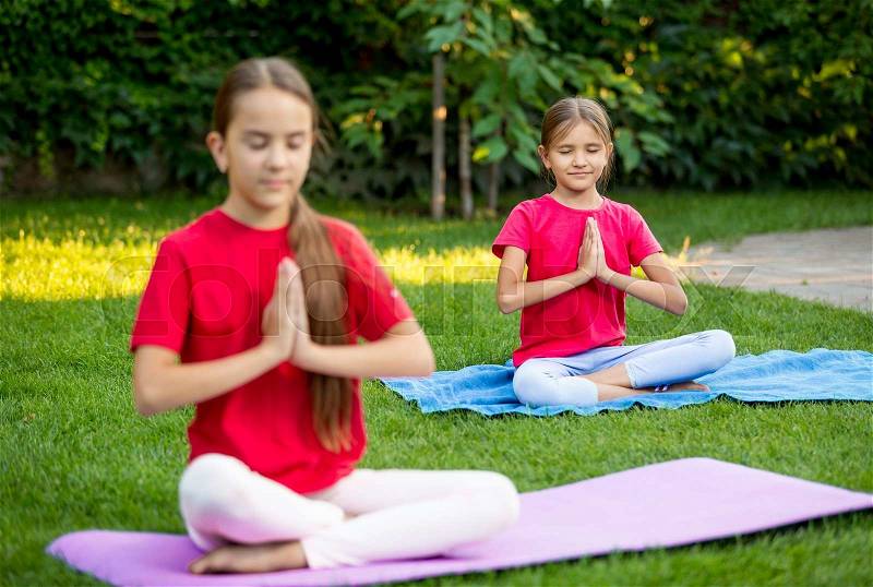 Two cute girls practicing yoga at park at hot sunny day, stock photo