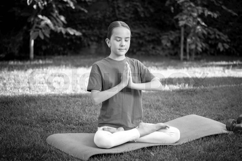 Black and white portrait of cute teen girl meditating at park, stock photo