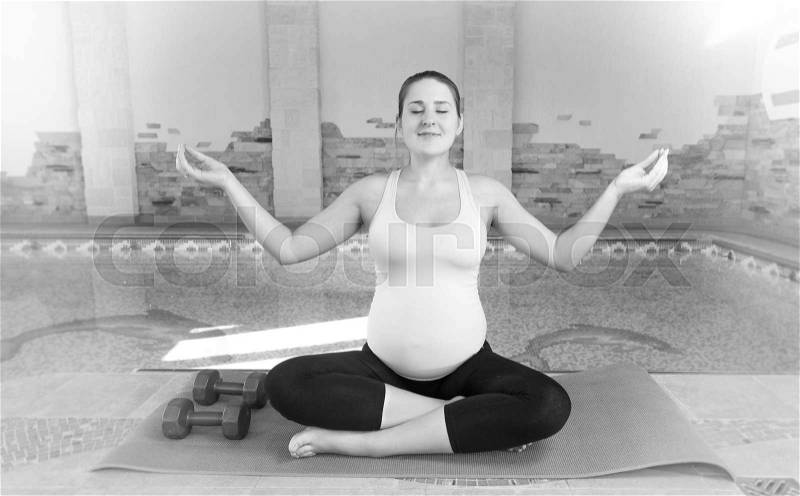 Black and white photo of pregnant woman doing yoga at fitness club, stock photo