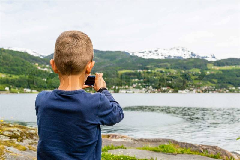 Young boy in Norway taking a picture of the surrounding scenery with his compact digital camera, stock photo