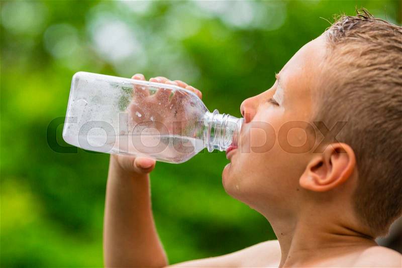 Closeup of young boy drinking fresh and clean cold tap water from transparent plastic drinking bottle while outdoors on a hot summer day, stock photo