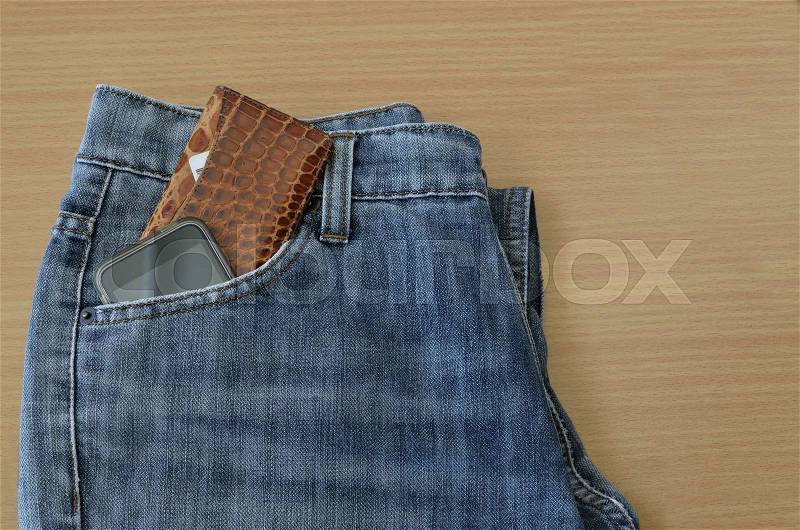 Leather wallet and smart phone in jeans pocket on wooden background, stock photo